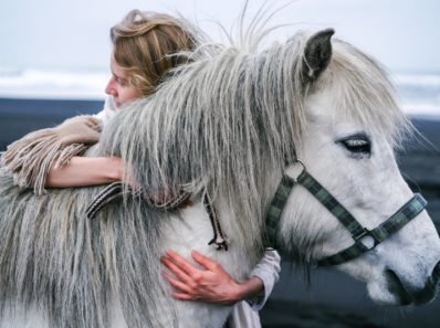 woman embracing gently gray horse on beach